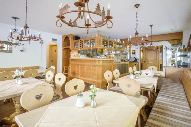 Helles Café mit Holztischen und Stühlen mit Herzschnitt, zentraler Bar und Kronleuchtern.