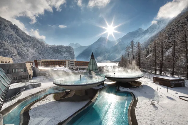 Winterlandschaft mit Thermalbad-Pools in einer Bergregion, Schnee, Berge und klare Sonne.