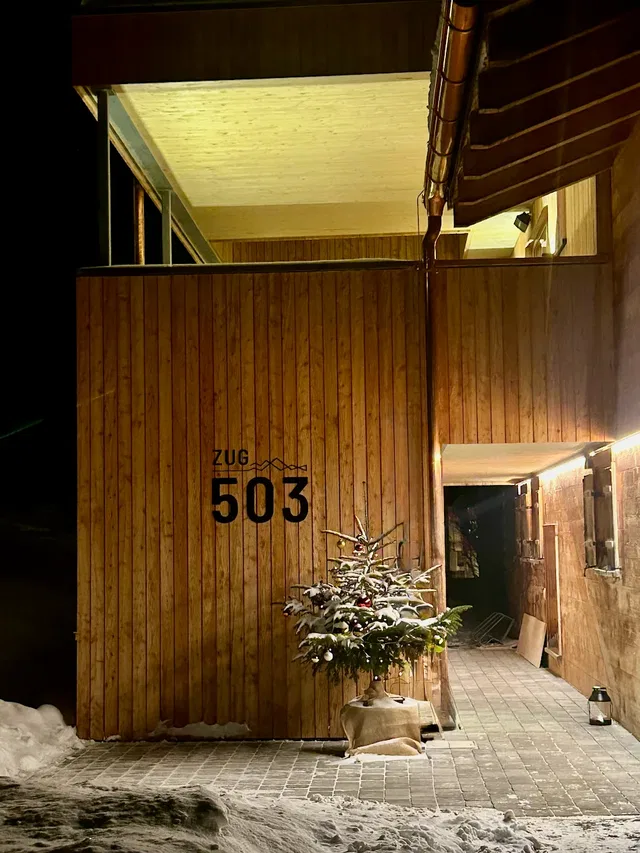 Holzeingang eines Gebäudes mit der Hausnummer 503 und verschneitem Baum