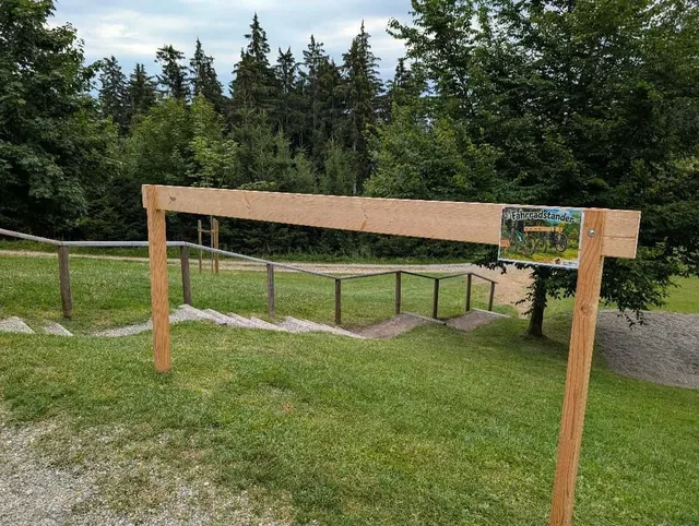 Holzbarriere am Weg mit Schild 'Fahrradständer' vor grünem Wald
