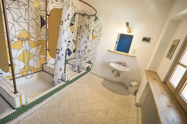 Badezimmer mit bunter Mosaikwand, Dusche, Waschbecken und Spiegel im sonnigen Raum.