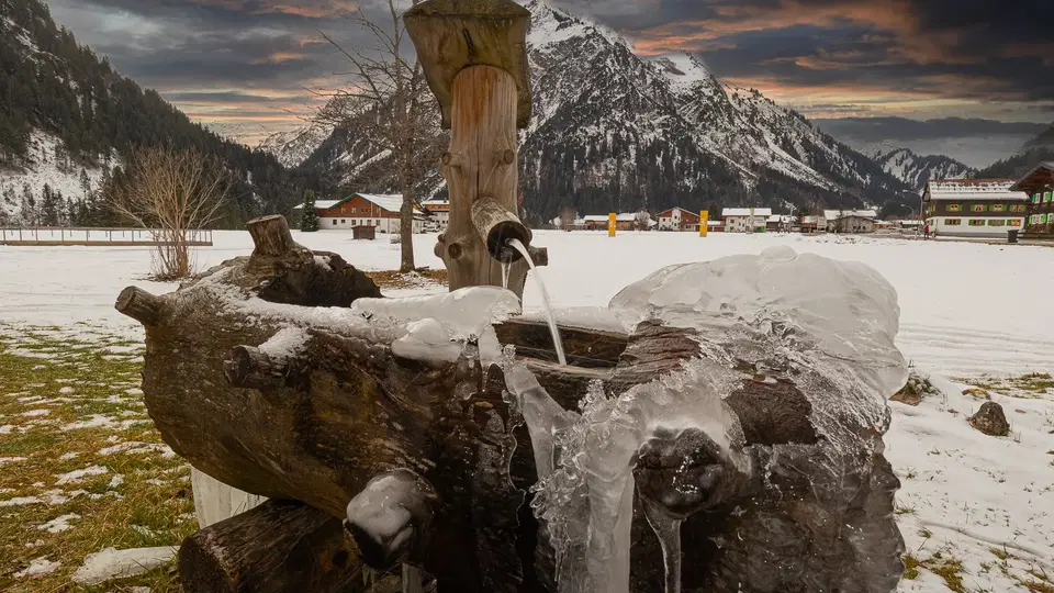 Holzbrunnen im Garten mit winterlichem Bergblick