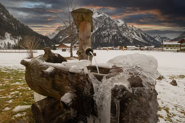 Holzbrunnen im Garten mit winterlichem Bergblick