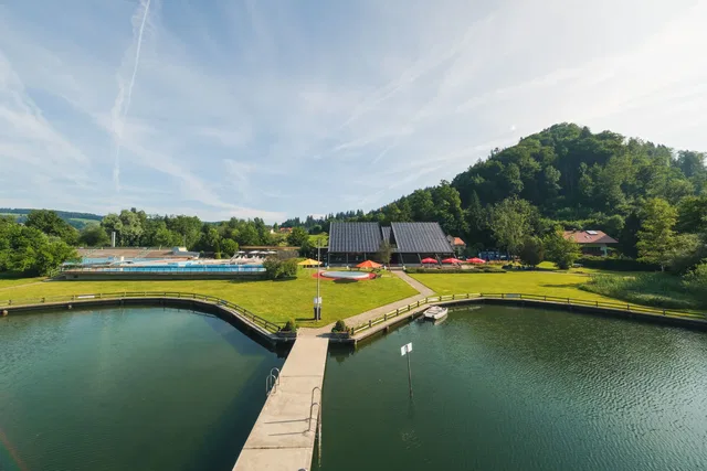 Blick über den Seezugang des Freibades mit Liegewiese, Schwimmbecken und Gebäuden.
