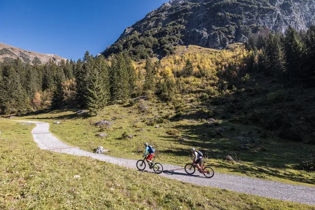 Zwei Mountainbiker auf einem Weg vor einer felsigen Bergflanke