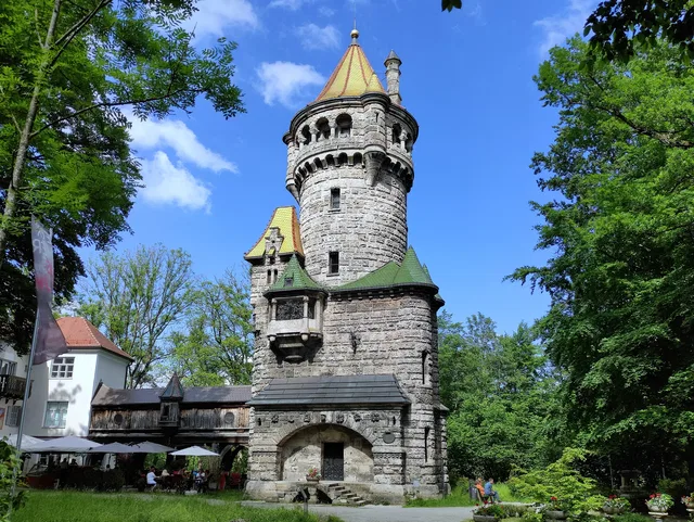 Historischer Steinturm mit gelb-grünen Dächern im Park, umgeben von Bäumen.