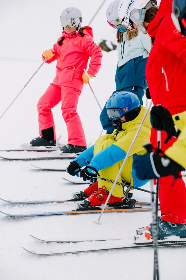 Gruppe Skifahrerinnen und Skifahrer in bunten Anzügen auf Skiern im Schnee