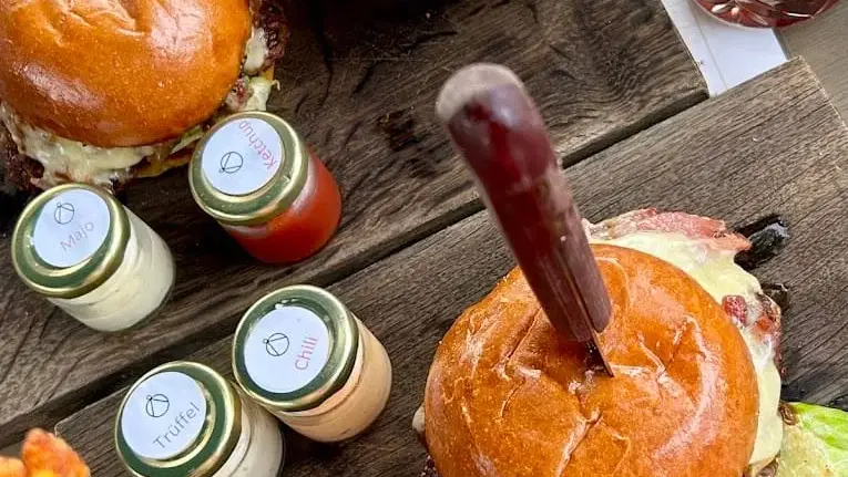 Zwei Burger mit Salat, Beilagen und Dip-Saucen auf Holztisch