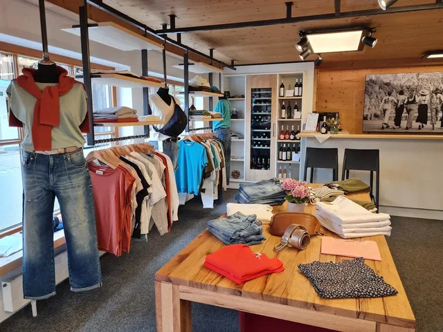 Modegeschäft mit Kleiderstangen, Mannequins und Holztisch, bunte Kleidung und Regale im Hintergrund.