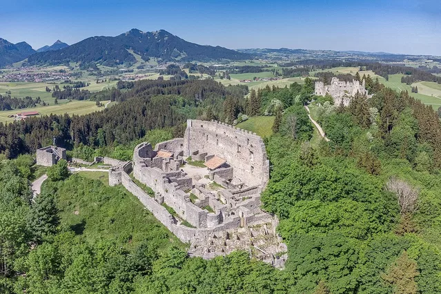 Historische Burgruine auf grüner Waldlandschaft mit Bergen im Hintergrund.