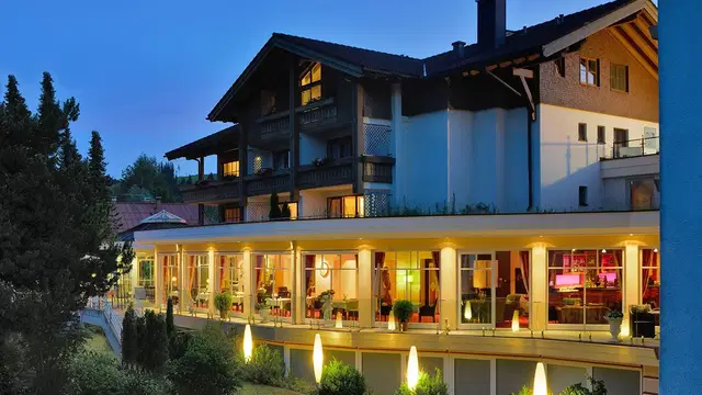 Mehrstöckiges Hotel mit verglaster Terrasse, abends warm beleuchtet.