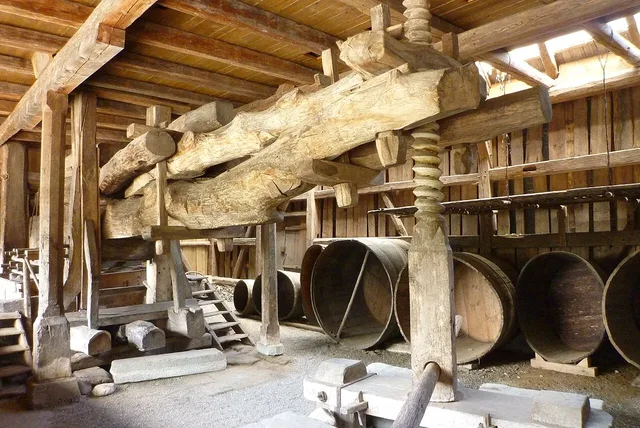 Historischer Holzturm mit schweren Balken und großen Holzfässern in einer Holzwerkstatt/Weinkeller.