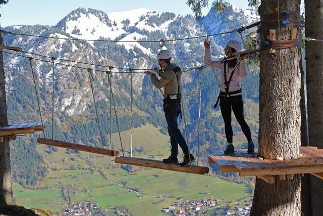 Zwei gesicherte Personen auf einer Hängebrücke im Kletterpark vor verschneiten Bergen