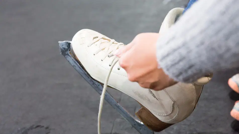 Weiße Schlittschuhe beim Zubinden der Schnürsenkel