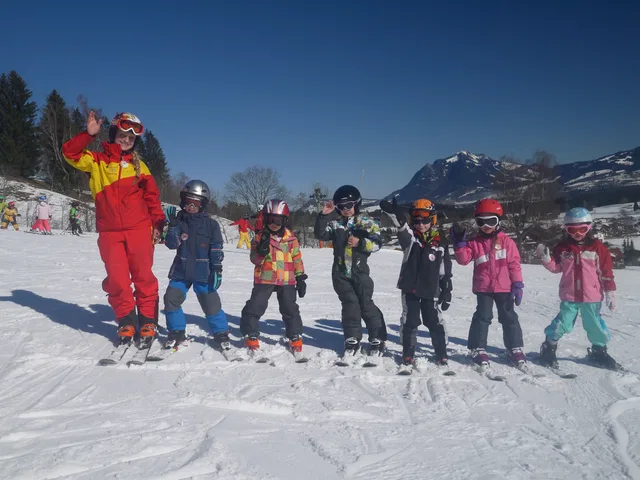 Kinder und eine erwachsene Person beim Skifahren vor verschneiten Bergen