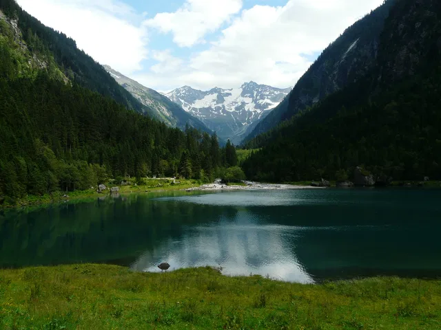Bergsee mit bewaldeten Hängen und schneebedeckten Gipfeln