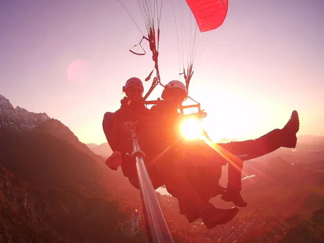 Zwei Paraglider im Sonnenuntergang über einer Berglandschaft.