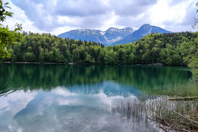 Kristallklarer See vor Wald und schneebedeckten Bergen