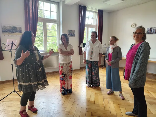 Fünf Frauen im Kreis in einem hellen Raum, eine spricht links, die anderen hören zu.