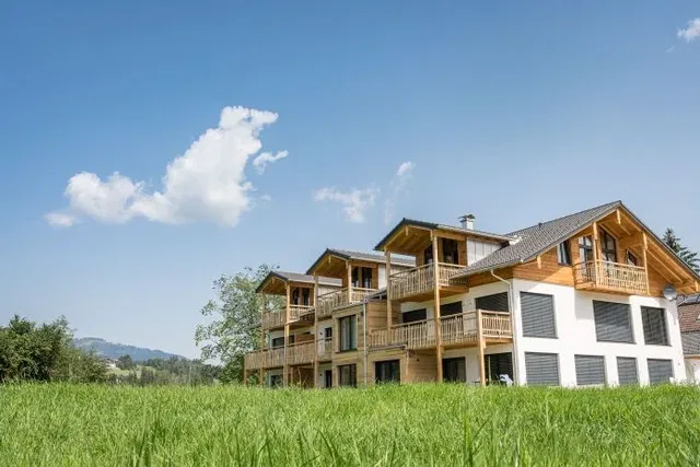 Mehrstöckiges Holzhaus mit Balkonen in einer grünen Wiese im Allgäu.