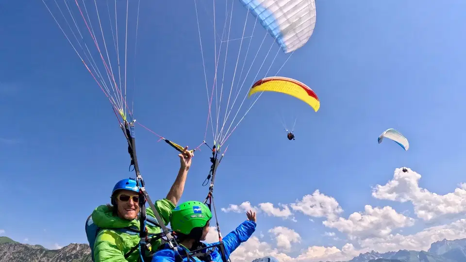 Tandemflug über grünen Bergkämmen mit einem weiteren Gleitschirm im Hintergrund