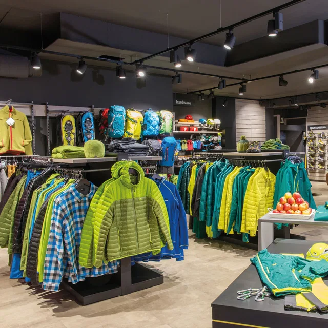 Innenansicht eines Outdoor-Geschäfts mit bunten Jacken, Rucksäcken und Produkten auf Regalen