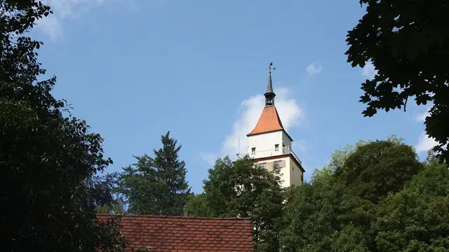 Weißer Gigelturm mit rotem Dach über grünen Bäumen vor blauem Himmel in Biberach. Ortsmotiv zur Ausflugsplanung.