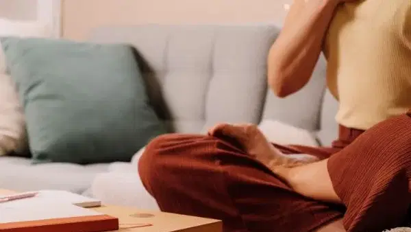 Person sitzt auf einer Couch, führt Atemübung durch, Hand auf der Brust.