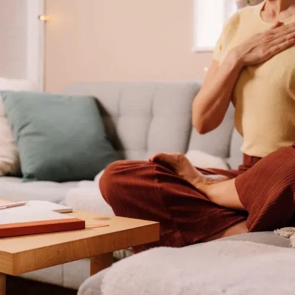 Person sitzt auf einer Couch, führt Atemübung durch, Hand auf der Brust.