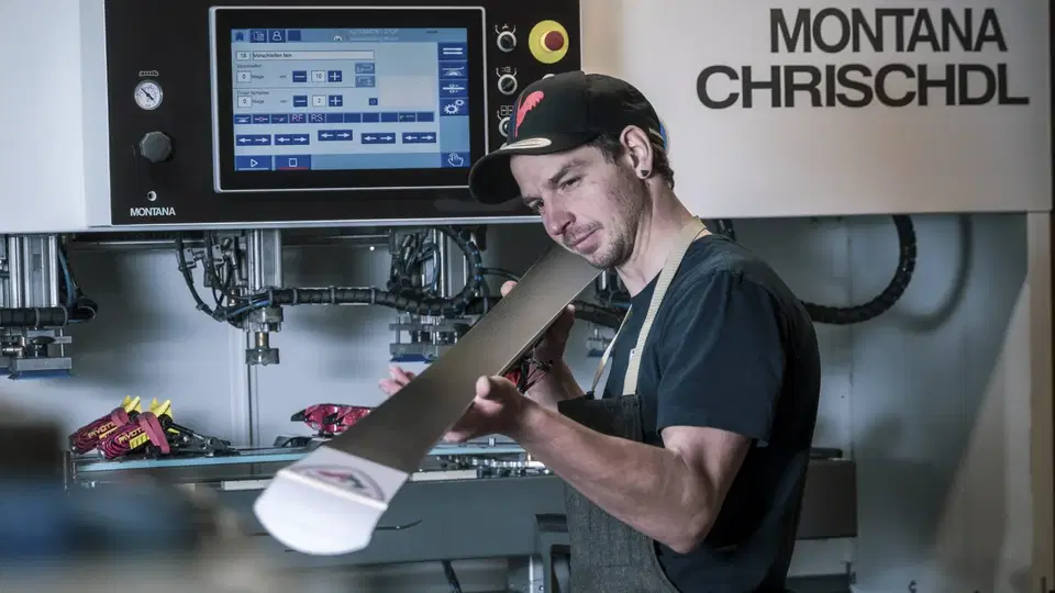 Mann mit Cap bedient eine Montana-Schneidemaschine beim Zuschnitt eines Holzstücks.