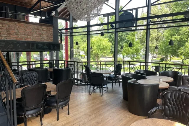 Gemütliches Restaurantinterieur mit schwarzen Ledersesseln, Holztischen und großen Glasfronten.