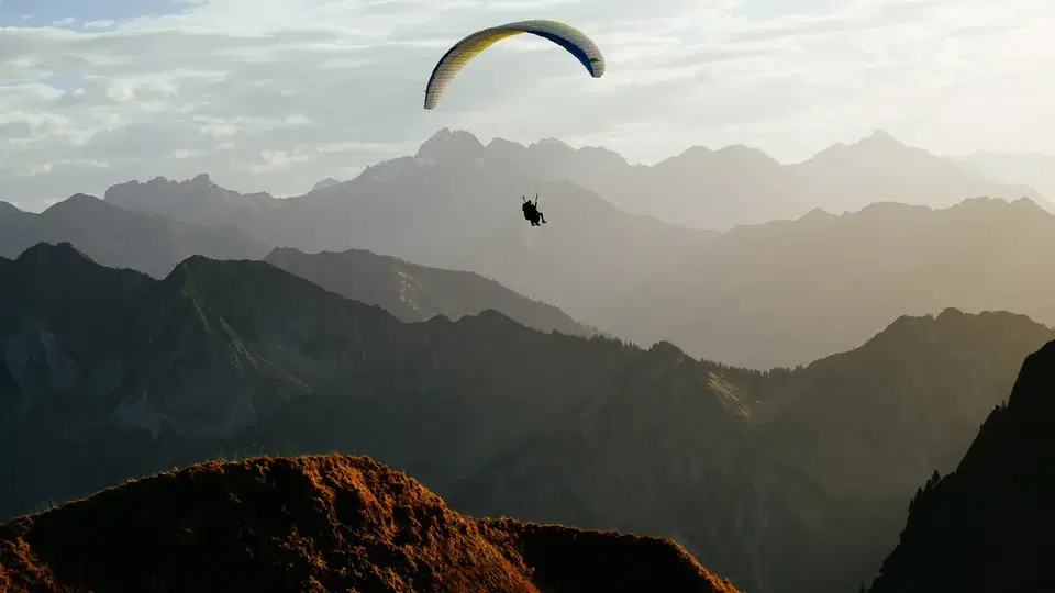 Gleitschirm vor mehreren Bergketten im Gegenlicht