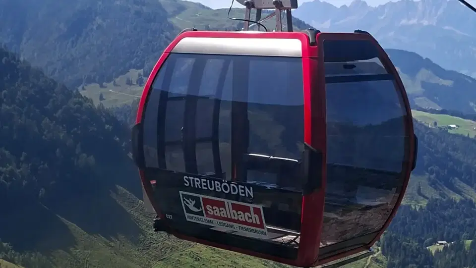 Rote Gondel der Seilbahn über einer grünen Berglandschaft