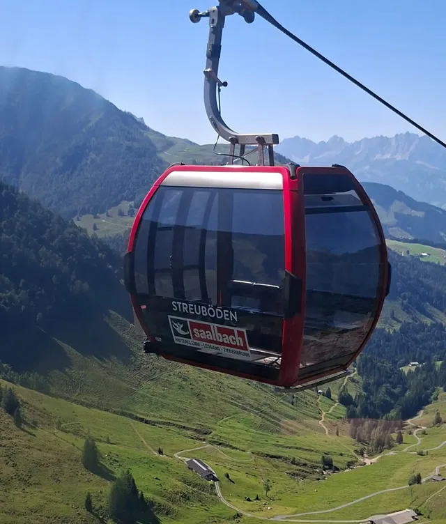 Rote Gondel der Seilbahn über einer grünen Berglandschaft