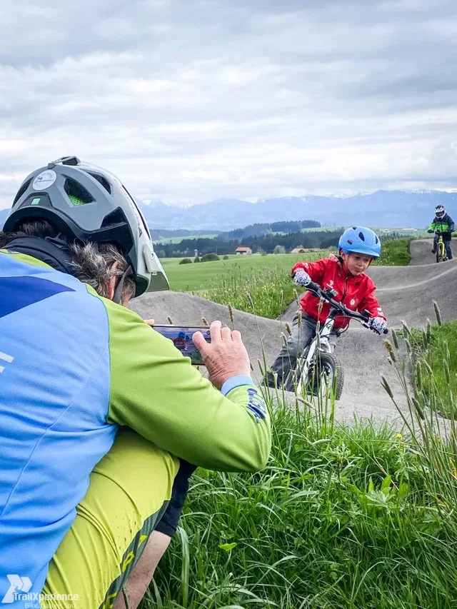 Kind fährt mit dem Mountainbike auf einem Pumptrack vor Berglandschaft