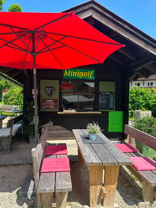Minigolf-Kiosk mit rotem Sonnenschirm und Sitzplätzen