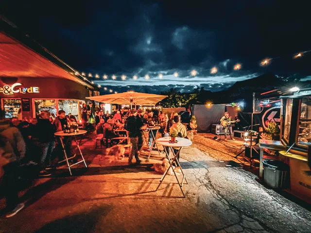 Abendliche Outdoor-Veranstaltung vor Food-Trucks, Musiker und Gäste bei Lichterketten