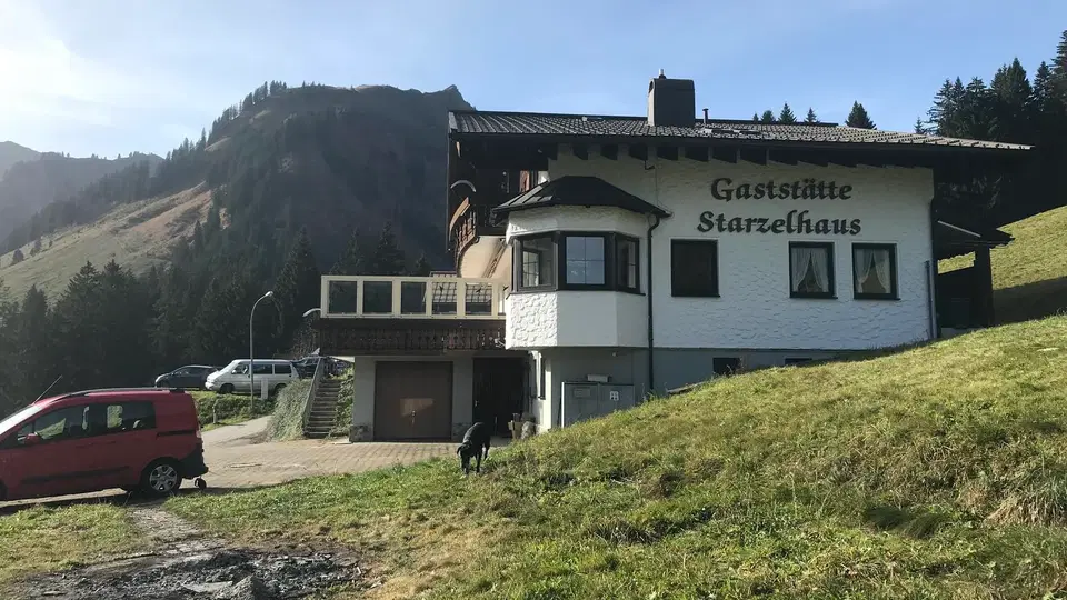 Gästehaus Starzelhaus vor Berghang mit Fahrzeugen am Parkplatz