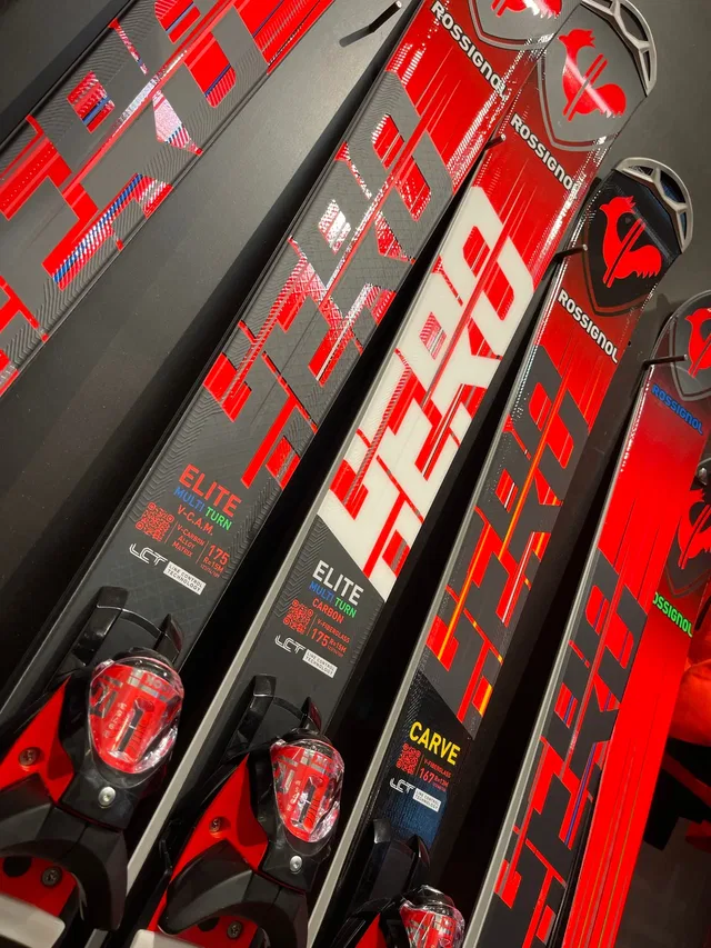 Mehrere Rossignol Elite Carve Skier in Rot-Schwarz im Regal, Bindungen sichtbar.