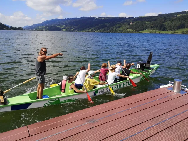 Drachenboot mit Paddlern auf einem See, Trainer stehend am Heck