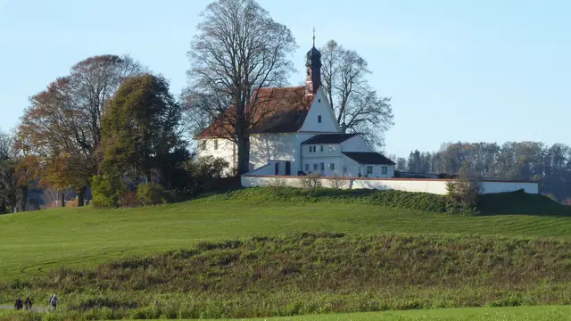 Die weiße Loretokapelle Wolfegg steht auf einem grünen Hügel zwischen herbstlichen Bäumen. Ortsmotiv zur Ausflugsplanung.