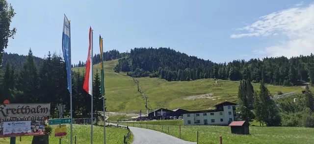 Landschaft mit Flaggenpfosten, Straße, Weideland und Chalet am Hang
