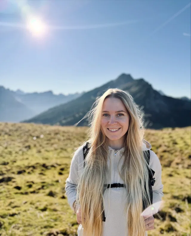 Junge Frau mit langen blonden Haaren vor Berglandschaft bei Sonnenschein