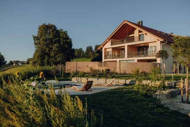 Chalet-ähnliches Haus mit Balkon, Garten und Poolbereich im Vordergrund.