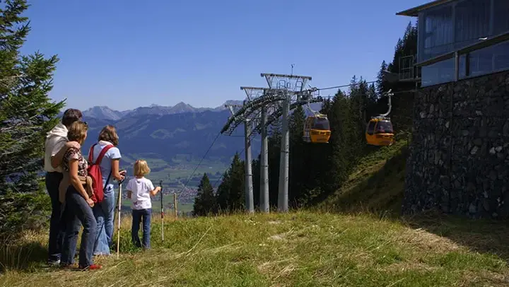 Familie neben der Bergstation mit gelben Gondeln der Hörnerbahn.