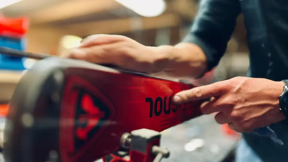 Nahaufnahme: Person bearbeitet ein rotes Snowboard in einer Werkstatt.