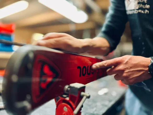 Nahaufnahme: Person bearbeitet ein rotes Snowboard in einer Werkstatt.