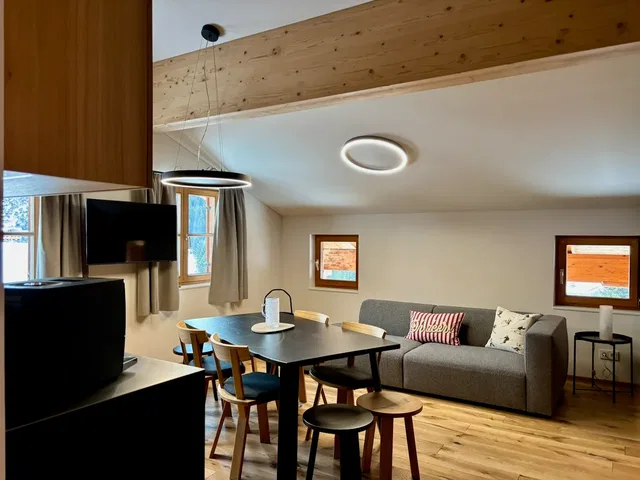 Wohnzimmer mit Holzbalken-Decke, runder Deckenleuchte, Esstisch und Sofa