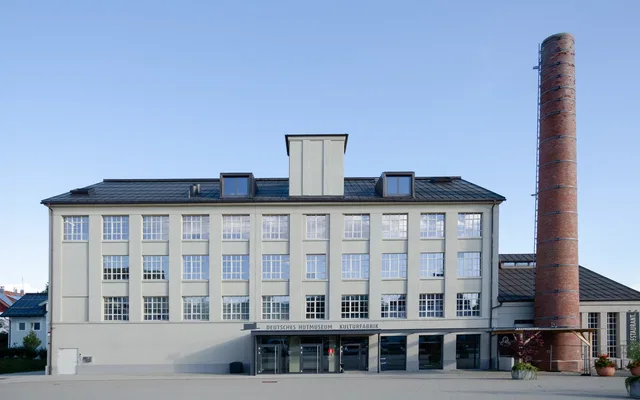 Hutmuseum-Gebäude mit rotem Ziegel-Schornstein vor freiem Vorplatz.