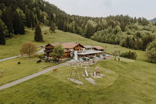Alpe Dornach mit Terrasse und Spielplatz am bewaldeten Hang.
